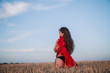 A young, slender, with loose hair in black panties in a field of wheat with a red dress in her hand.