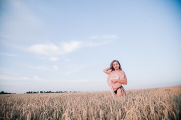 A young, slender, in black panties in a field of wheat covers her chest with a straw hat.