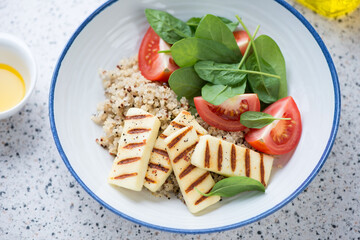 Quinoa with grilled halloumi cheese, fresh spinach and red tomatoes served in a white plate, middle close-up, studio shot
