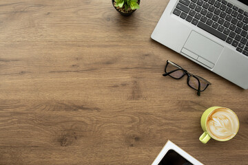 Wood office desk table with laptop computer, cup of latte coffee and office supplies. Top view with...