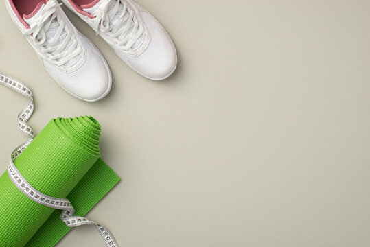Sports concept. Top view photo of tape measure green exercise mat and white sneakers on isolated pastel grey background with empty space
