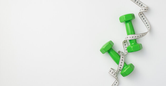Slimming concept. Top view photo of green dumbbells and tape measure on isolated white background with copyspace
