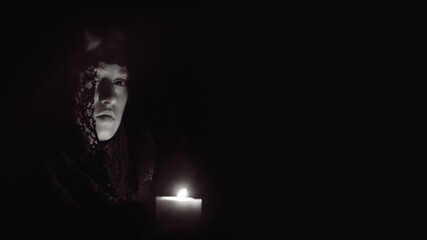 Woman in a black hood with a lit candle in her hands, black and white photo