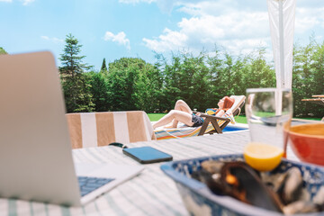 Scene of a table on the terrace of a house in summer with a woman lying by the pool in the background. Summer scene, outdoor dining. copy space and graphic resources.