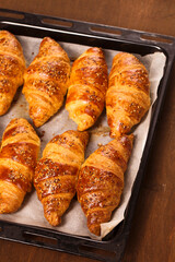 big croissants in a metal baking sheets on a wooden background