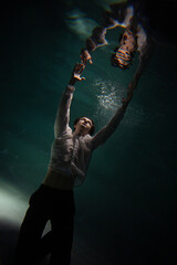 underwater shooting with contrasting light, a guy is swimming underwater, pulling his hand to his...