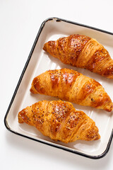 Three croissants on a white baking tray, top view