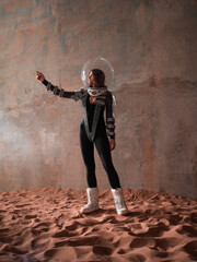 An astronaut on a desert planet alone, an explorer on a distant planet, other worlds and civilizations. A young woman in a retrofuturism-style spacesuit stands on the sand and looks around © Ulia Koltyrina