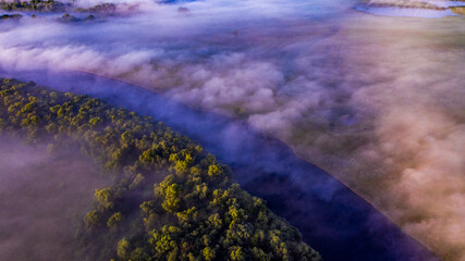 Fototapeta na wymiar Aerial view of a beautiful summer landscape with a fog while dawn. Photo from drone of a foggy landscape in spring. Top view to land while sunrise. Early morning in nature, misty weather.