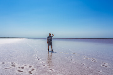 A man stands on dried salt on the shore of a lake, looking into the distance. An unusual natural phenomenon is a lake with red salt water on the site of an extinct mud volcano.