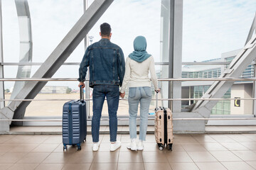 Fototapeta Rear View Of Muslim Couple Standing With Luggage Near Window At Airport obraz