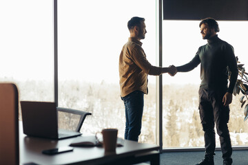 Two serious businessmen shaking hands, making deal or agreement at contemporary office, empty space