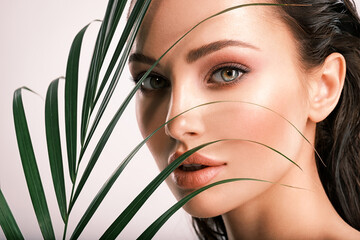 Young beautiful woman with green leaves near face. Skin care beauty treatments concept.  Closeup girl's face with green leave.