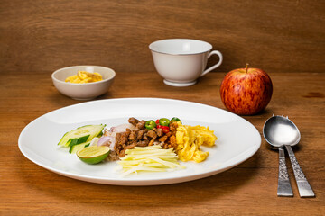 High angle view of shrimp paste fried rice with sweet pork, fried egg and other in white ceramic dish with a cup of coffee and ripe red apple on wooden table. - Powered by Adobe