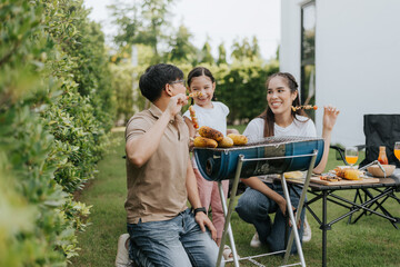 Asian family having dinner in the backyard at home. Happy family with little child camping and have fun in house backyard outside. Barbecue time, Family activities conccept.