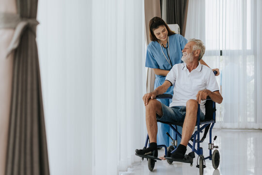 Young asian nurse helping senior man at home. Elderly man sitting on wheelchair and talking with young docter in house. Senior health care.