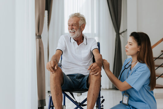 Young asian nurse helping senior man at home. Elderly man sitting on wheelchair and talking with young docter in house. Senior health care.