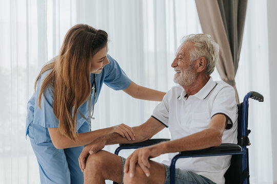 Young asian nurse helping senior man at home. Elderly man sitting on wheelchair and talking with young docter in house. Senior health care.