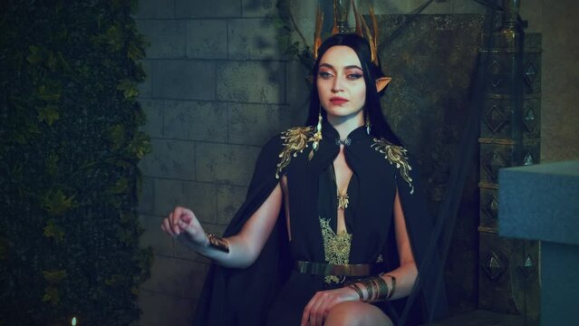 Portrait fantasy gothic woman queen sits on throne, holds white barn owl on hand. Bird flaps wings, flies away. Princess girl sexy vampire, carnival costume, black dress golden crown, old style room