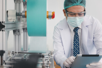 Doctor engineer or scientist in face mask using computer tablet working with medical mask production machine factory