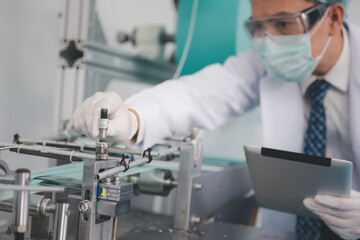 Doctor engineer or scientist in face mask using computer tablet working with medical mask production machine factory