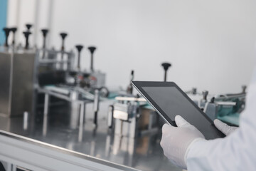 Doctor engineer or scientist using computer tablet working with medical mask production machine in a manufacturing factory