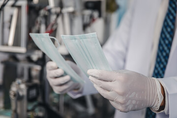 Obraz premium Doctor hand in glove holding checking face mask at a production machine manufacturing factory
