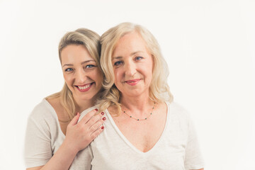 Blonde caucasian attractive woman in her 40s wearing white T-shirt looking at camera, the other woman standing behind her and hugging her. Studio shot. High quality photo