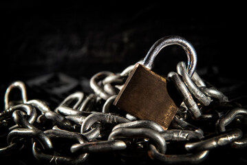 Stacked metal chain with closed padlock on dark background
