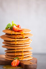 Pancakes for breakfast. Cover with pancakes. A stack of pancakes on a wooden board with honey. Honey pours on pancakes. Dessert. Favorite breakfast. Beautiful food cover.American breakfast. 
