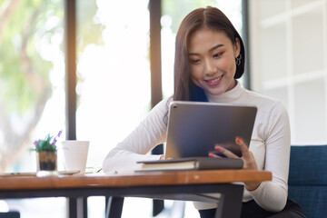 Attractive young Asian business woman wearing casual clothes is working on a tablet in the home office.