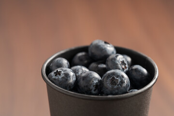 Blueberries in black paper cup on walnut table