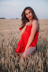 A young, slender girl with loose hair in a field of wheat covers her naked body with a red dress.