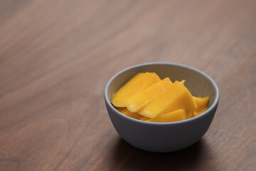 Fresh sliced mango in a ceramic bowl on walnut table