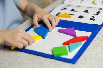 The tangram is wooden. The child plays with developing wooden eco-friendly toys. The concept of children's education