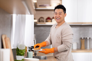 Cheerful chinese man washing dishes at home