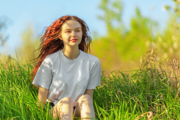 Beautiful ginger-haired girl on green meadow grass
