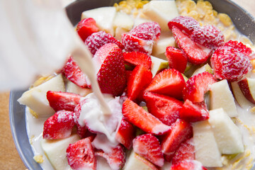 Cornflakes with fruit - apple, pear and strawberries - with oat milk being poured