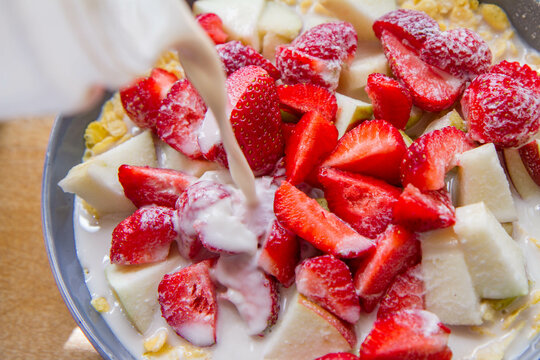 Cornflakes with fruit - apple, pear and strawberries - with oat milk being poured