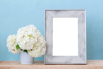 White flowers in a vase and an empty photo frame on a table on a blue background