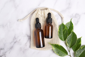 Unbranded serum bottles on cotton bag with leaves on marble background. Hyaluronic acid oil, serum with collagen and peptides skin care product. Mockup packaging, cosmetic design branding