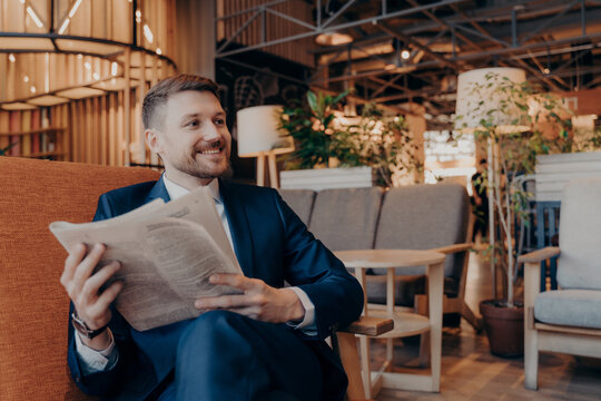 Positive young businessman reading newspaper in cafe