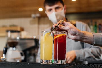 Two stylish bartenders in masks and uniforms are preparing cocktails at a party during a pandemic. The work of restaurants and cafes during the pandemic.
