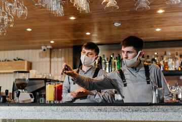 Two stylish bartenders in masks and uniforms are preparing cocktails at a party during a pandemic. The work of restaurants and cafes during the pandemic.