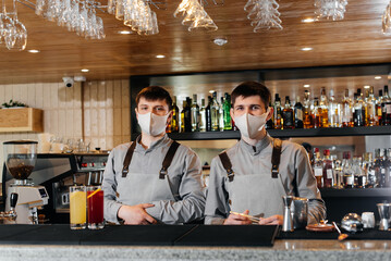 Two stylish bartenders in masks and uniforms are preparing cocktails at a party during a pandemic. The work of restaurants and cafes during the pandemic.