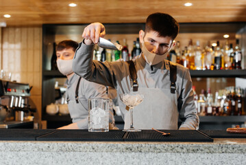 Two stylish bartenders in masks and uniforms are preparing cocktails at a party during a pandemic. The work of restaurants and cafes during the pandemic.