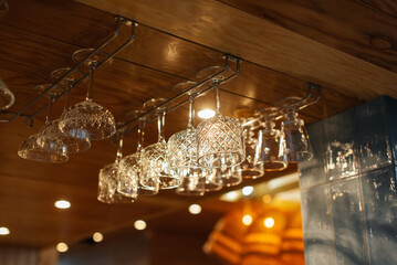 Stylish glasses for various alcoholic beverages hang over the bar in a modern restaurant. Glasses...