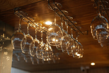 Stylish glasses for various alcoholic beverages hang over the bar in a modern restaurant. Glasses...