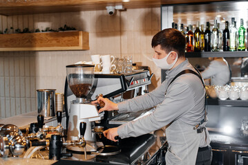 A masked barista prepares an exquisite delicious coffee at the bar in a coffee shop. The work of restaurants and cafes during the pandemic.