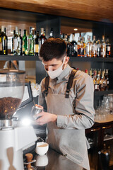 A masked barista prepares an exquisite delicious coffee at the bar in a coffee shop. The work of restaurants and cafes during the pandemic.
